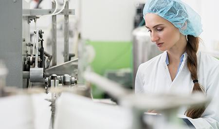 韦德注册平台工业——快乐的女员工戴着防护帽和白色的实验室大褂，在一个现代工厂作为制造工程师工作